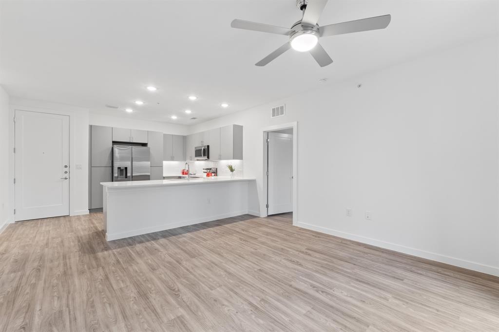 4801 Springdale Road, Unit 2010 Austin, TX 78723 - Photo 23 of 34 Open-concept living area featuring wood-finish flooring, a contemporary ceiling fan, and a kitchen with gray cabinetry, stainless steel appliances, and an island with a white countertop