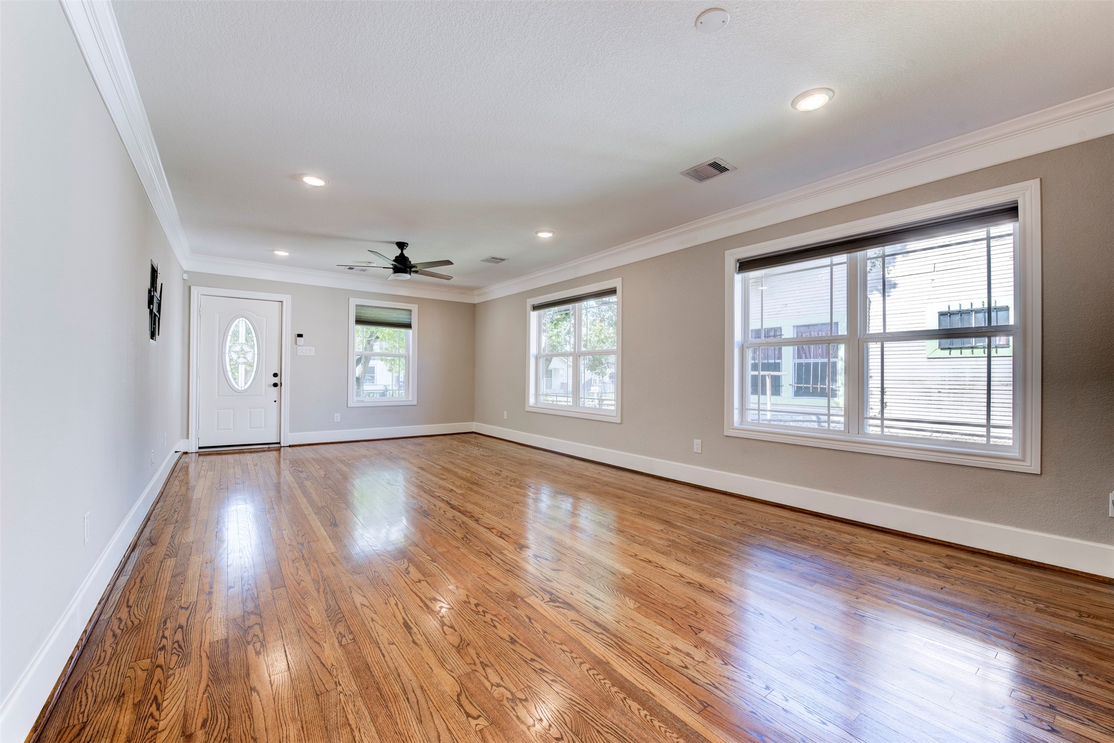 109 Dresden Street Houston, TX 77012 - Photo 6 of 43 Spacious living room with polished hardwood floors, large windows for natural light, neutral walls, and a ceiling fan. It features recessed lighting and a stylish front door with an oval window.