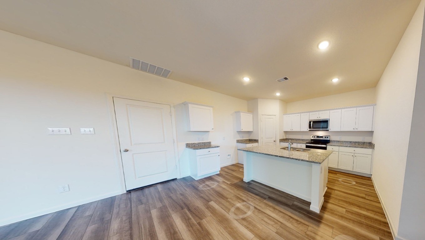 384 Enforcer Loop Jarrell, TX 76537 - Photo 9 of 15 Kitchen with white cabinets, a center island with sink, light wood-type flooring, stainless steel appliances, and light stone countertops
