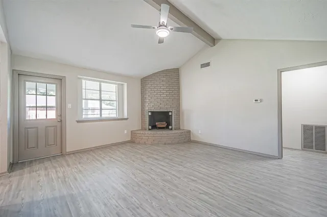 an empty room with wooden floor fireplace and windows