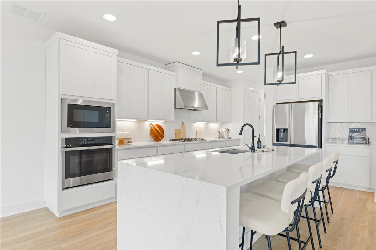 8700 Olmsted Way Austin, TX 78744 - Photo 12 of 40 Kitchen featuring stainless steel appliances, a kitchen breakfast bar, light wood-type flooring, hanging light fixtures, and white cabinets