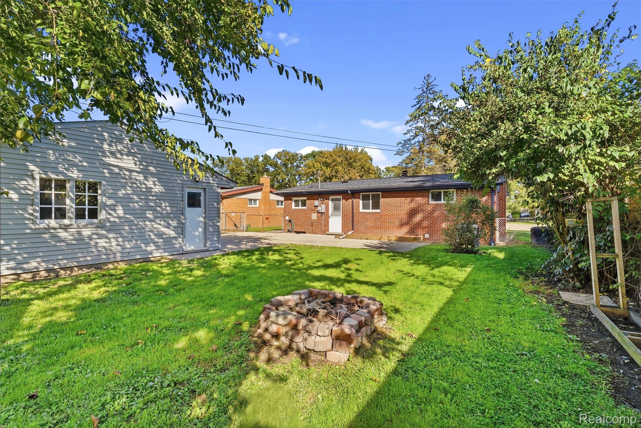 9101 Merriman Road Livonia, MI 48150 - Photo 36 of 41 Expansive backyard featuring a brick fire pit, manicured lawn, and mature trees