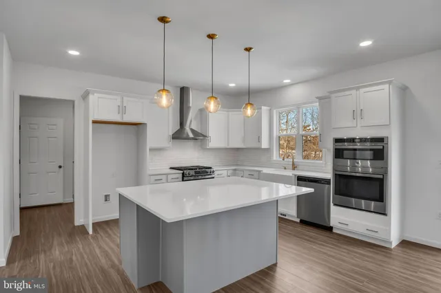 a kitchen with stainless steel appliances a stove a sink a refrigerator a center island a rug and wooden floor