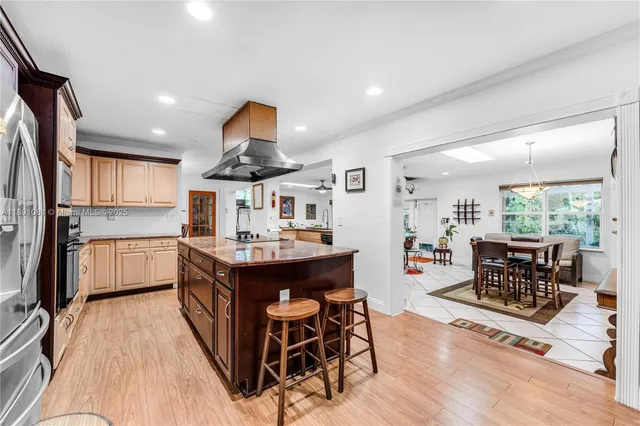 a kitchen with stainless steel appliances granite countertop a refrigerator a sink dishwasher a dining table and chairs with wooden floor