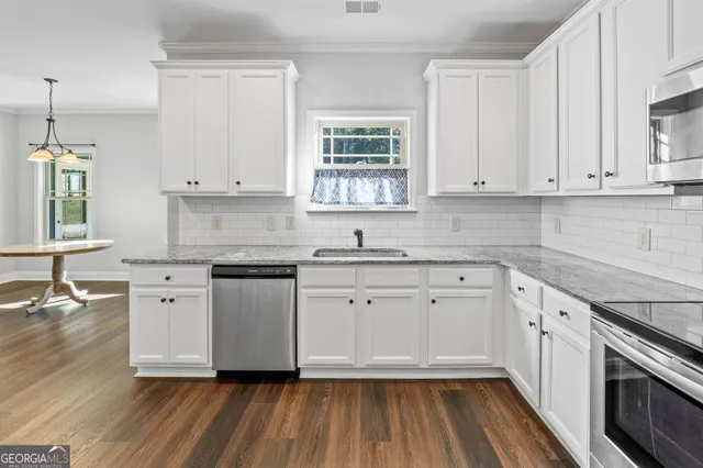 a kitchen with granite countertop a refrigerator a sink dishwasher a stove and white cabinets with wooden floor