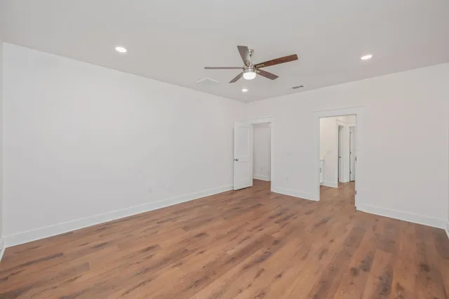 a view of an empty room with wooden floor and a ceiling fan
