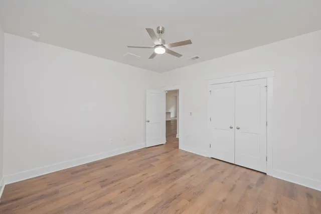 an empty room with wooden floor ceiling fan and window