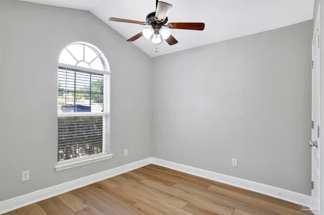 an empty room with wooden floor chandelier fan and windows
