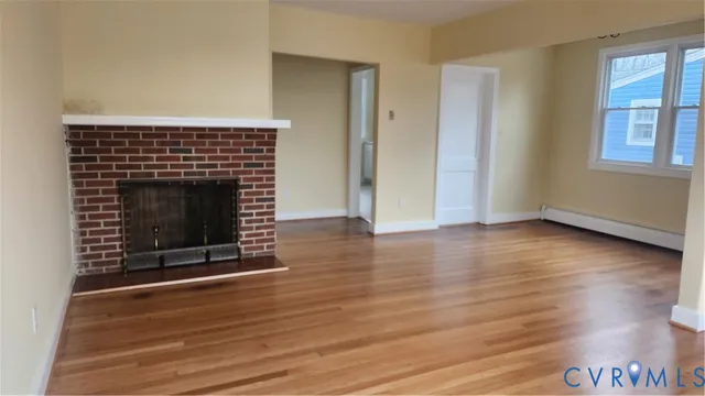 a view of an empty room with wooden floor fireplace and a window