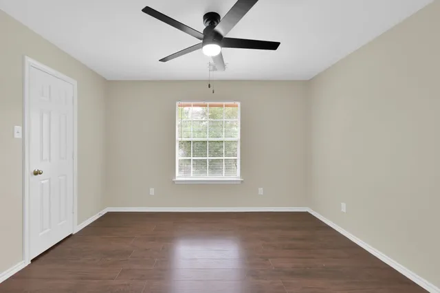 an empty room with wooden floor ceiling fan and windows