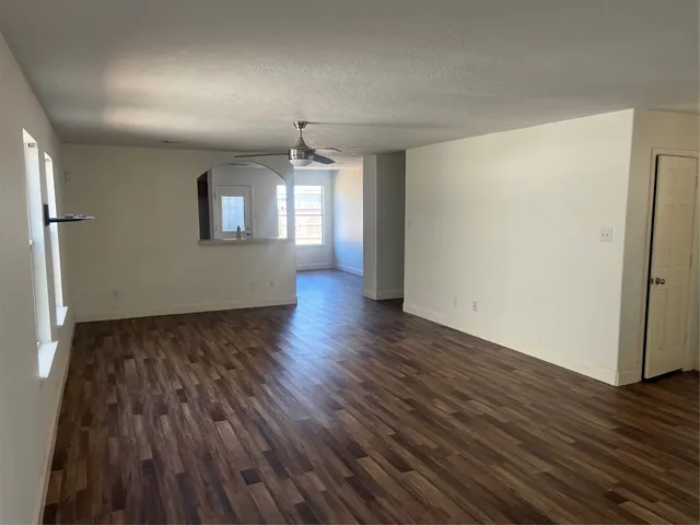 an empty room with wooden floor a ceiling fan and windows