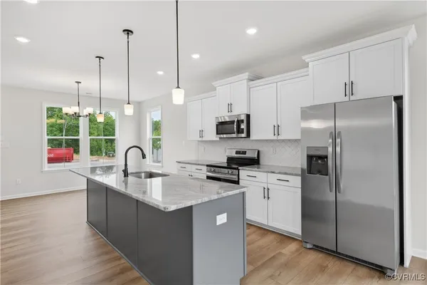 a kitchen with stainless steel appliances granite countertop a sink a stove a refrigerator a center island and a wooden floor