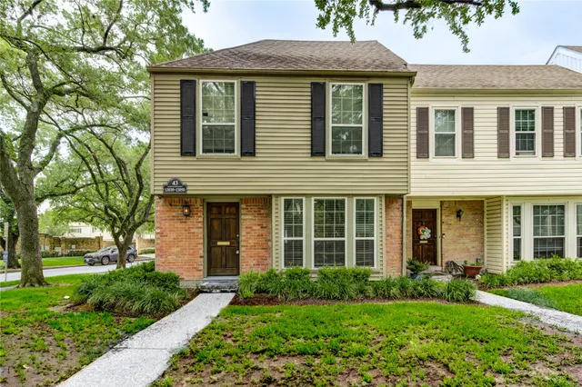 a view of a brick house with a yard plants and a large tree