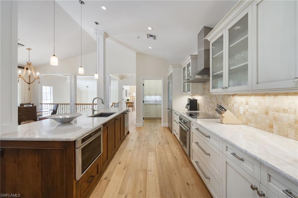 611 10th Avenue South, Unit B2 Naples, FL 34102 - Photo 11 of 27 Kitchen with light wood-type flooring, light stone counters, hanging light fixtures, glass insert cabinets, and white cabinets