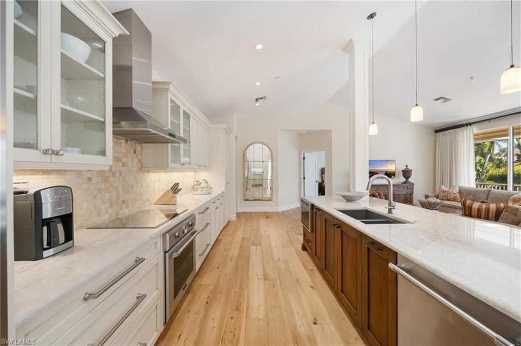 611 10th Avenue South, Unit B2 Naples, FL 34102 - Photo 12 of 27 Kitchen featuring appliances with stainless steel finishes, glass insert cabinets, light stone countertops, wall chimney exhaust hood, and light wood-style floors