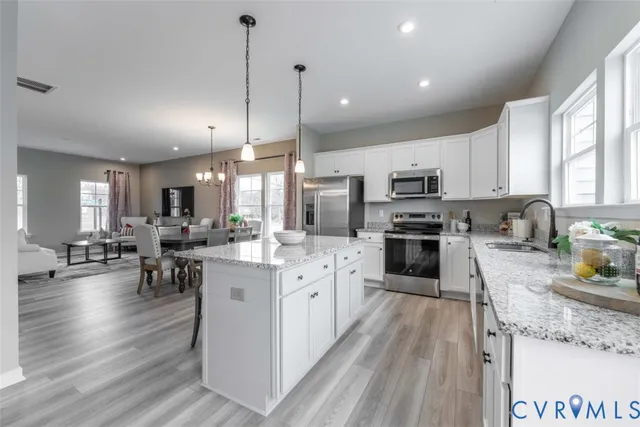 a kitchen with stainless steel appliances granite countertop a refrigerator a stove top oven a sink a dining table and chairs with wooden floor