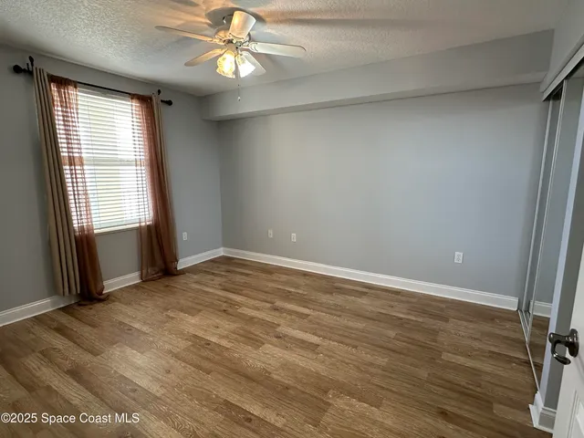 an empty room with wooden floor fan and windows