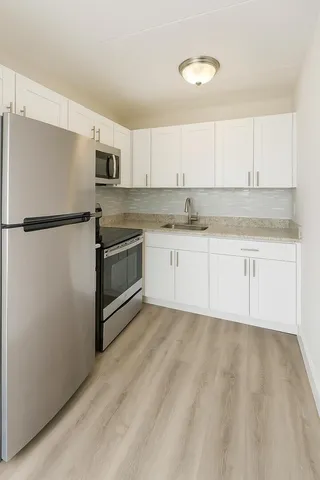 a kitchen with granite countertop a refrigerator a sink and white cabinets
