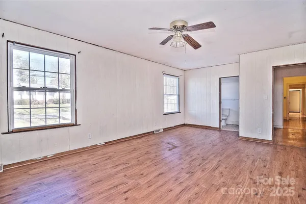 an empty room with wooden floor fan and windows