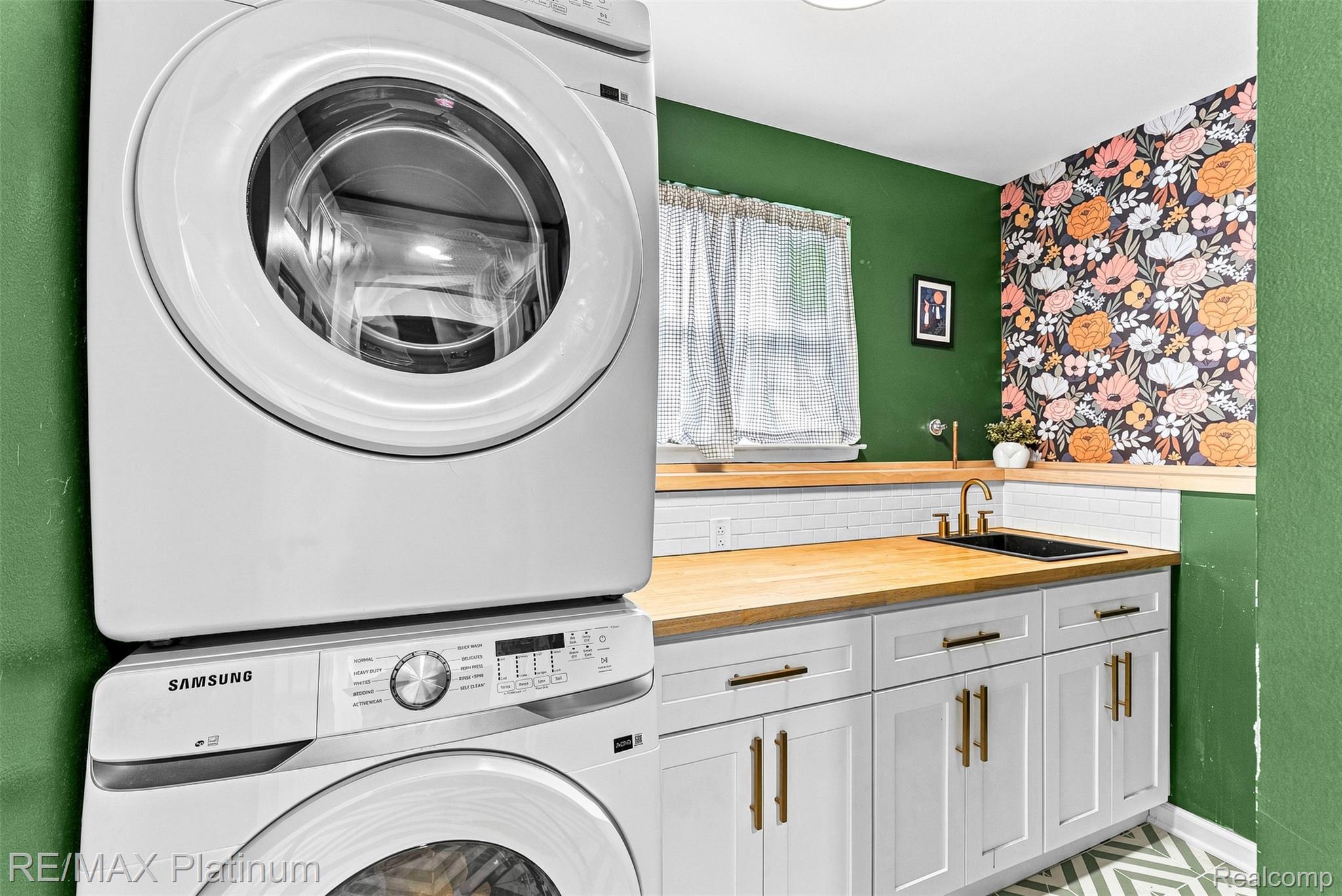 815 Oak Ridge Court Brighton, MI 48116 - Photo 32 of 37 Stackable washer and dryer, wood-finish countertops, undermount sink with brass-finish faucet, white shaker cabinetry with brass-finish hardware, and patterned accent wall