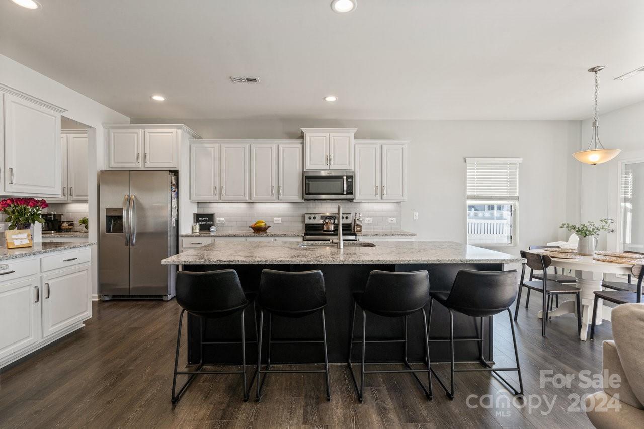 a kitchen with stainless steel appliances granite countertop a dining table chairs stove refrigerator and cabinets