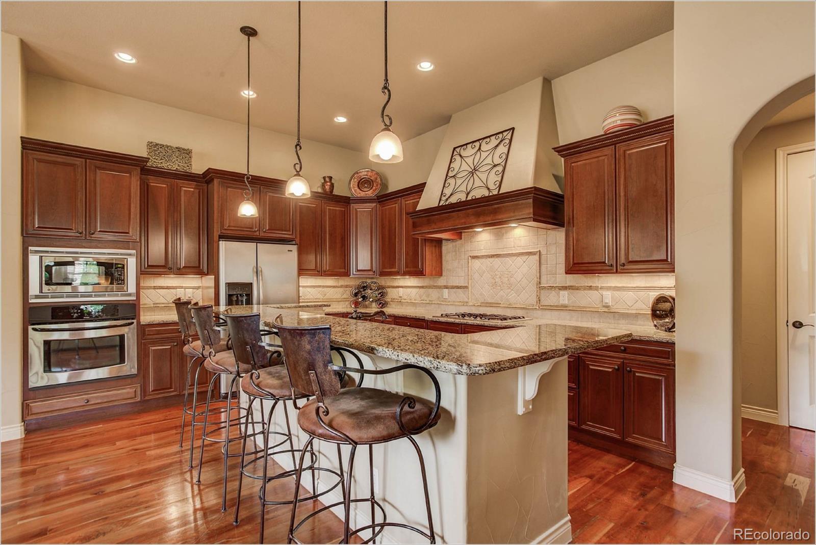 4363 Chateau Ridge Lane Castle Rock, CO 80108 - Photo 7 of 32 a kitchen with stainless steel appliances granite countertop a stove a sink a oven a dining table and chairs with wooden floor