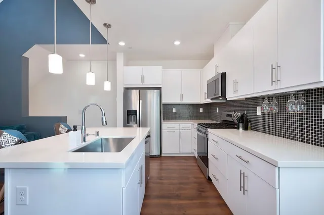 a kitchen with stainless steel appliances a sink dishwasher a refrigerator oven and white cabinets with wooden floor