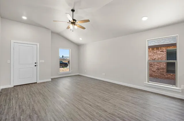an empty room with wooden floor chandelier fan and windows