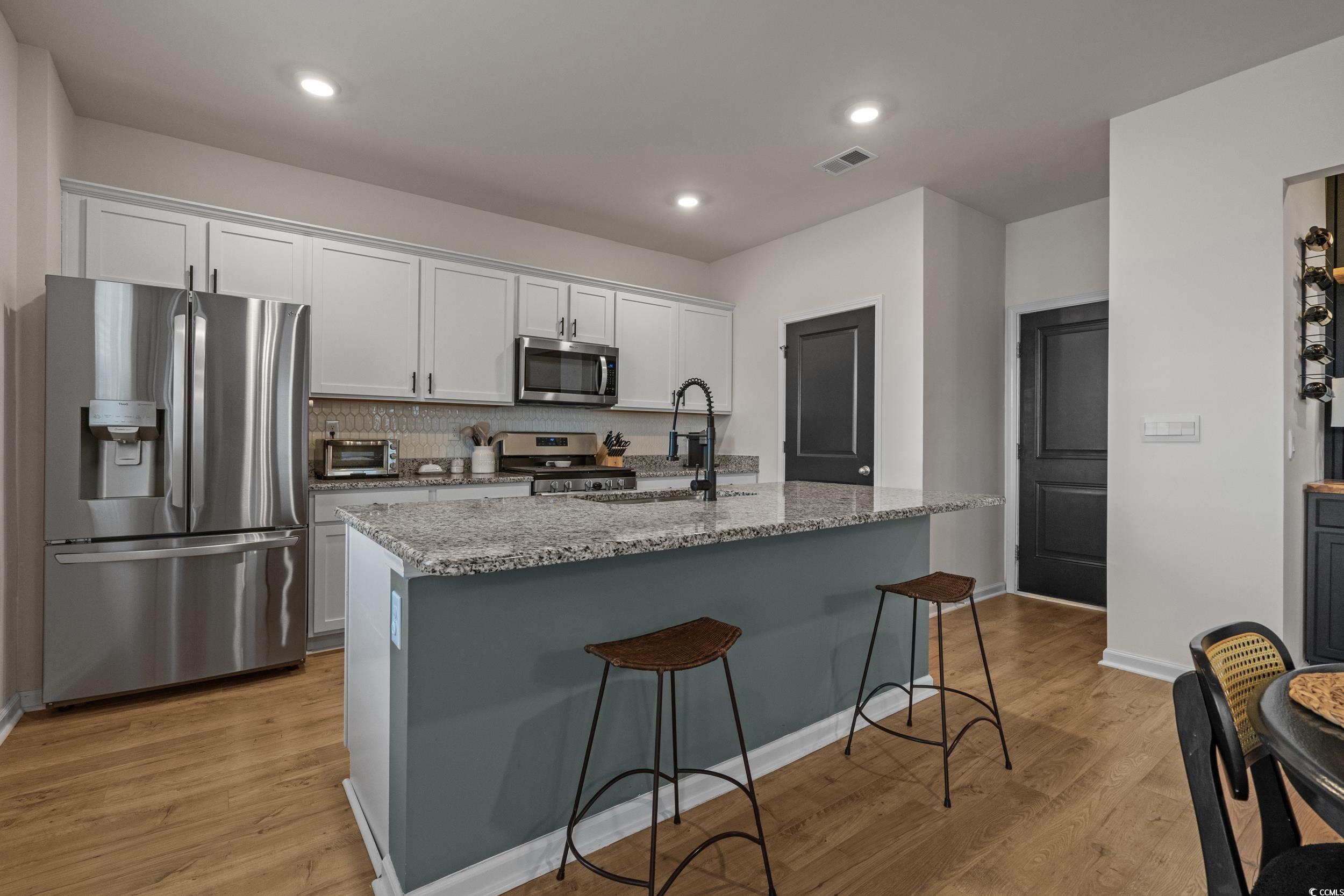 3343 Bells Lake Circle Longs, SC 29568 - Photo 12 of 40 Kitchen featuring stainless steel appliances, light stone counters, a kitchen breakfast bar, backsplash, and white cabinetry
