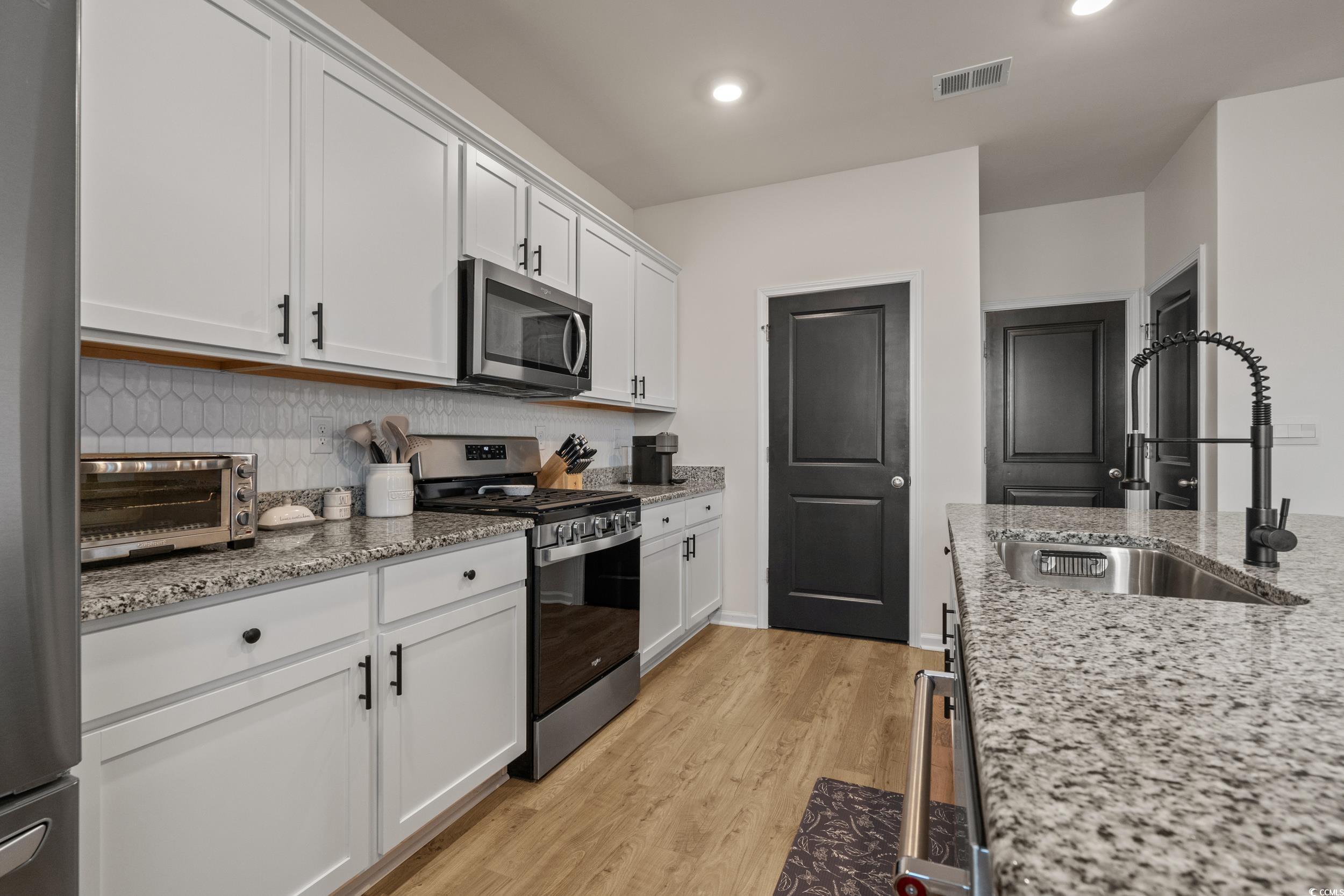 3343 Bells Lake Circle Longs, SC 29568 - Photo 13 of 40 Kitchen with stainless steel appliances, light stone counters, white cabinetry, light wood finished floors, and tasteful backsplash