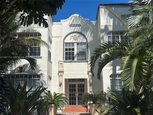 a view of a white building with potted plants and a large tree