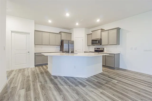 a large kitchen with kitchen island white cabinets stainless steel appliances a sink and a refrigerator