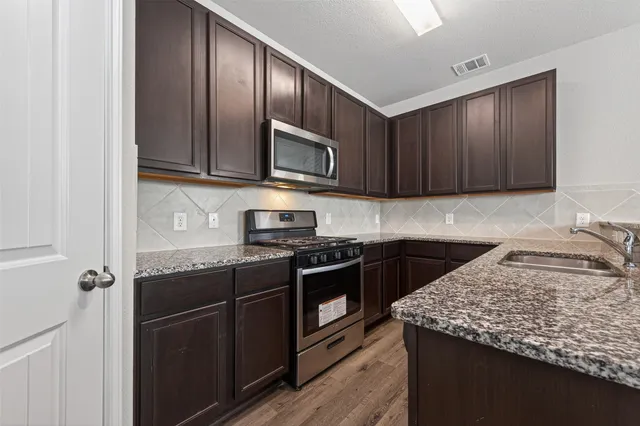 a kitchen with stainless steel appliances granite countertop wooden cabinets a stove top oven a sink and dishwasher