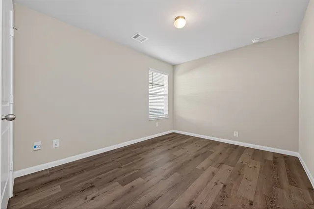 a view of an empty room with wooden floor and window