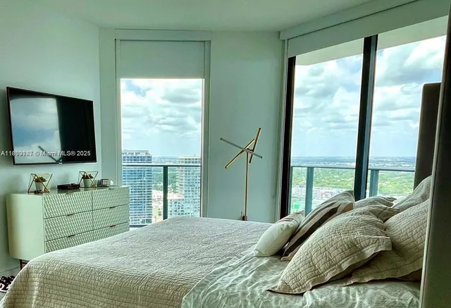 a bedroom with a bed television and a large window