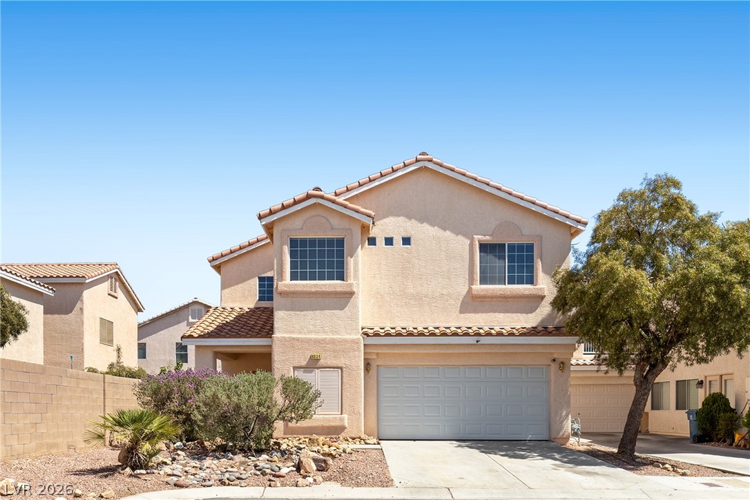 A cream-colored stucco home features a two-car garage and a tiled roof.