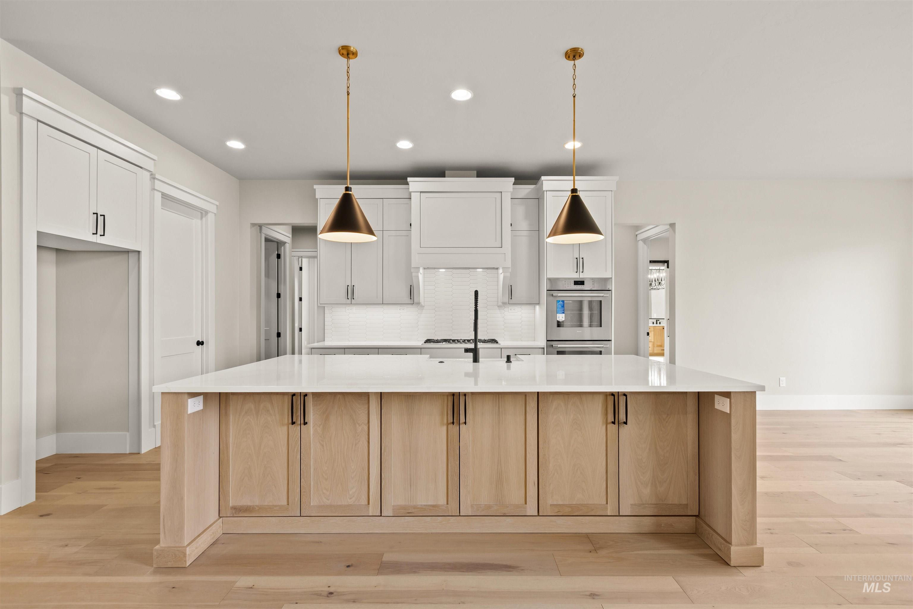 6891 South Utmost Way Meridian, ID 83642 - Photo 16 of 46 Kitchen featuring a large island with sink, tasteful backsplash, light wood-style floors, light stone counters, and light brown cabinetry