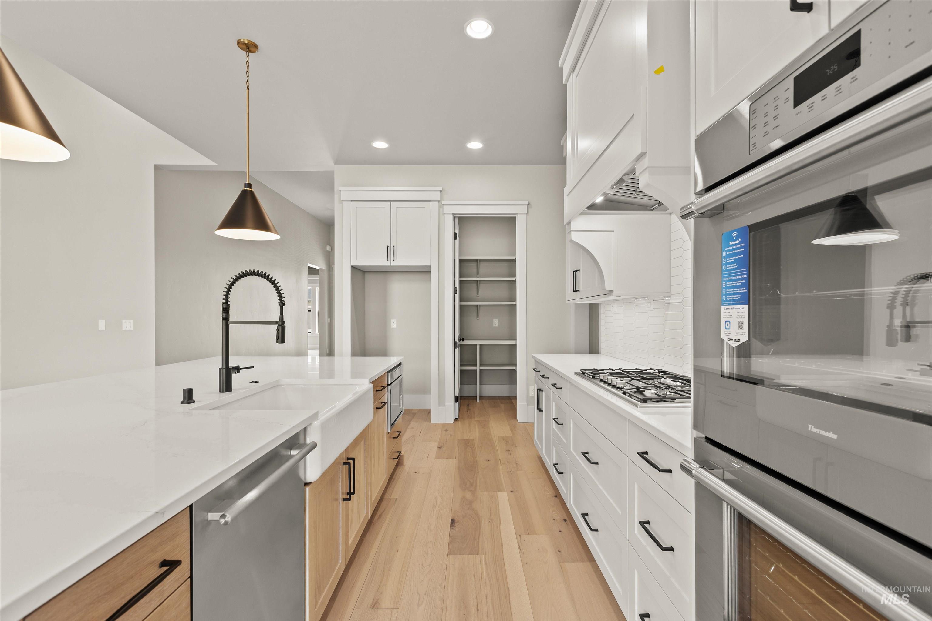 6891 South Utmost Way Meridian, ID 83642 - Photo 19 of 46 Kitchen with stainless steel appliances, white cabinets, recessed lighting, light wood finished floors, and hanging light fixtures
