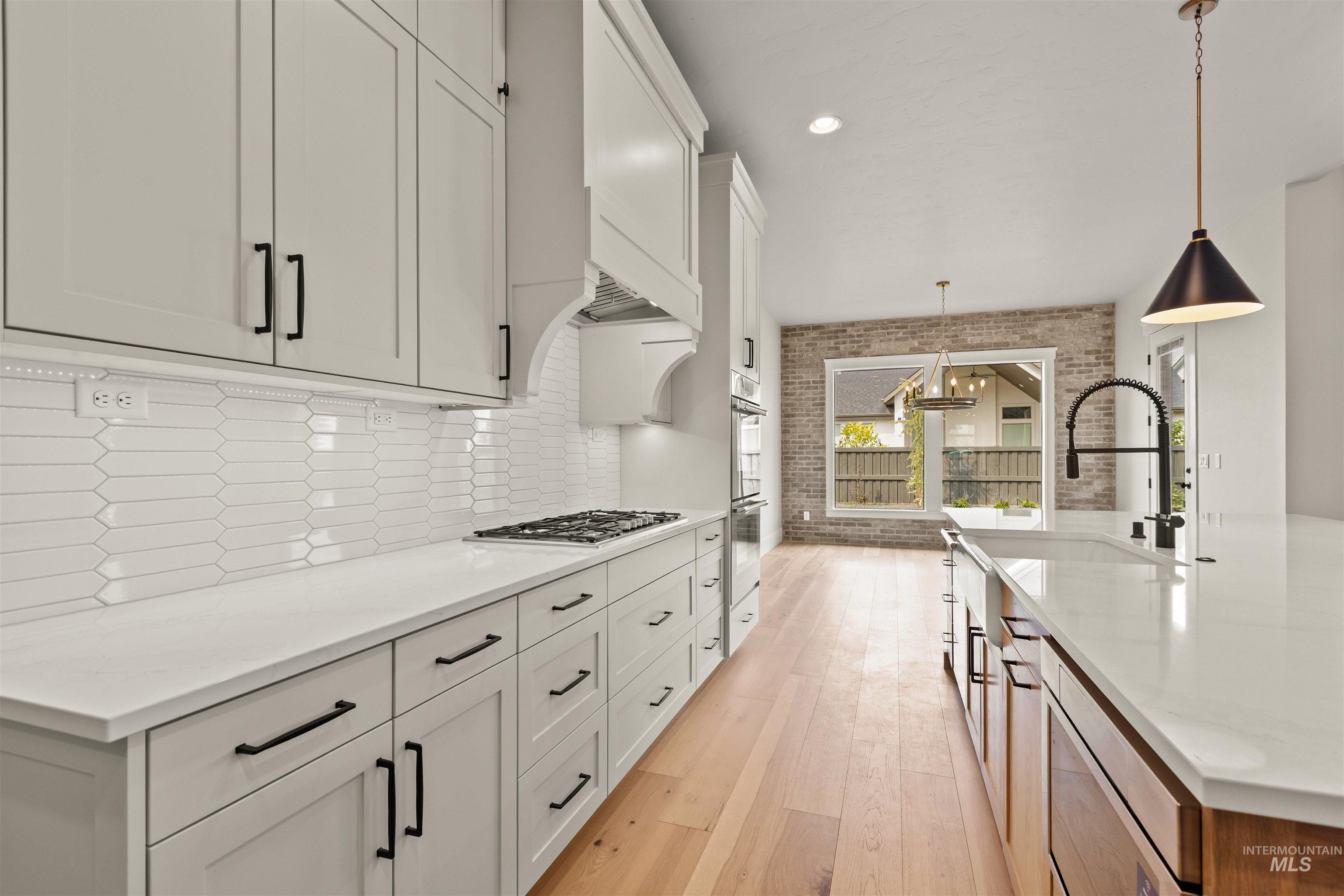 6891 South Utmost Way Meridian, ID 83642 - Photo 21 of 46 Kitchen with light wood-type flooring, hanging light fixtures, light stone countertops, white cabinets, and brick wall