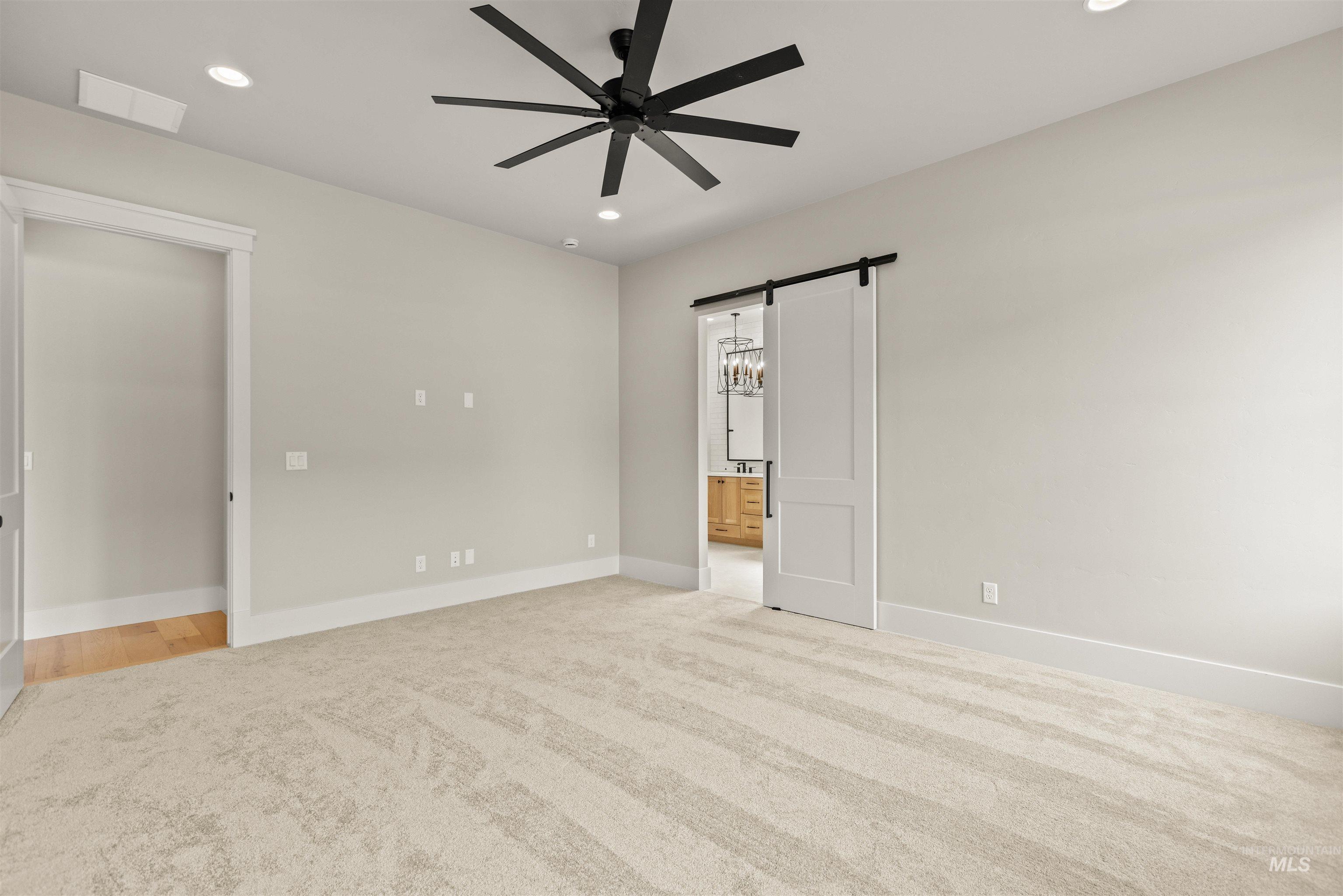 6891 South Utmost Way Meridian, ID 83642 - Photo 27 of 46 Unfurnished bedroom featuring a barn door, recessed lighting, light colored carpet, a ceiling fan, and ensuite bathroom