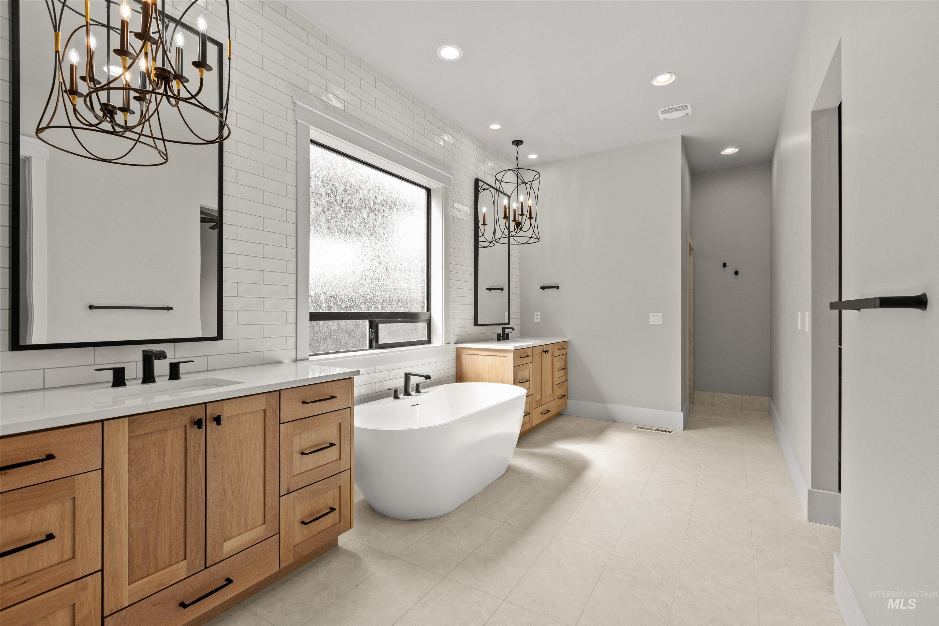 6891 South Utmost Way Meridian, ID 83642 - Photo 31 of 46 Bathroom featuring a chandelier, two vanities, a soaking tub, recessed lighting, and decorative backsplash