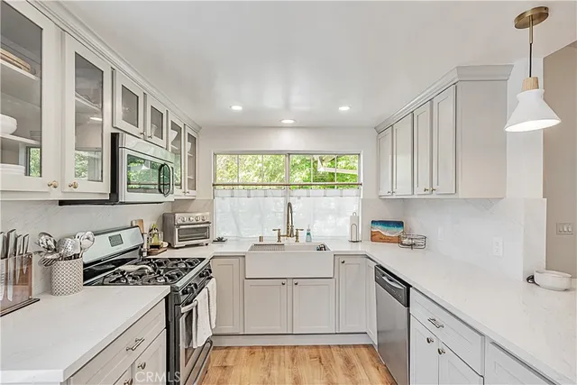 a kitchen with stainless steel appliances kitchen island granite countertop a stove a sink a refrigerator and white cabinets with wooden floor