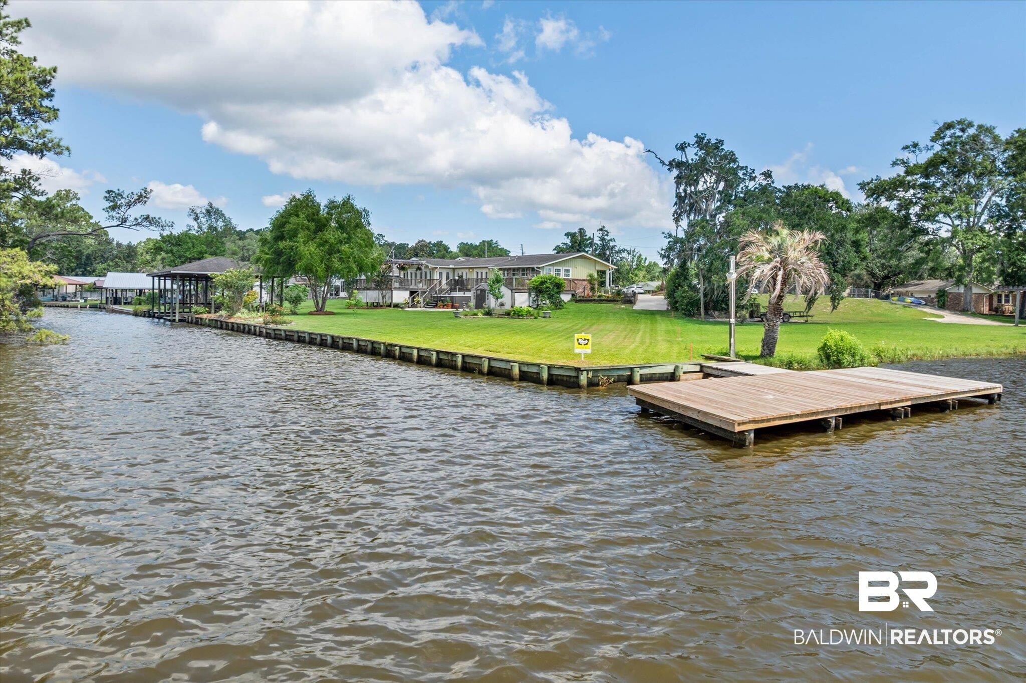 3801 Point Road Mobile, AL 36619 - Photo 52 of 55 Waterfront property featuring a wood-plank dock, a covered boat slip, a retaining wall, and a sloped lawn with mature trees