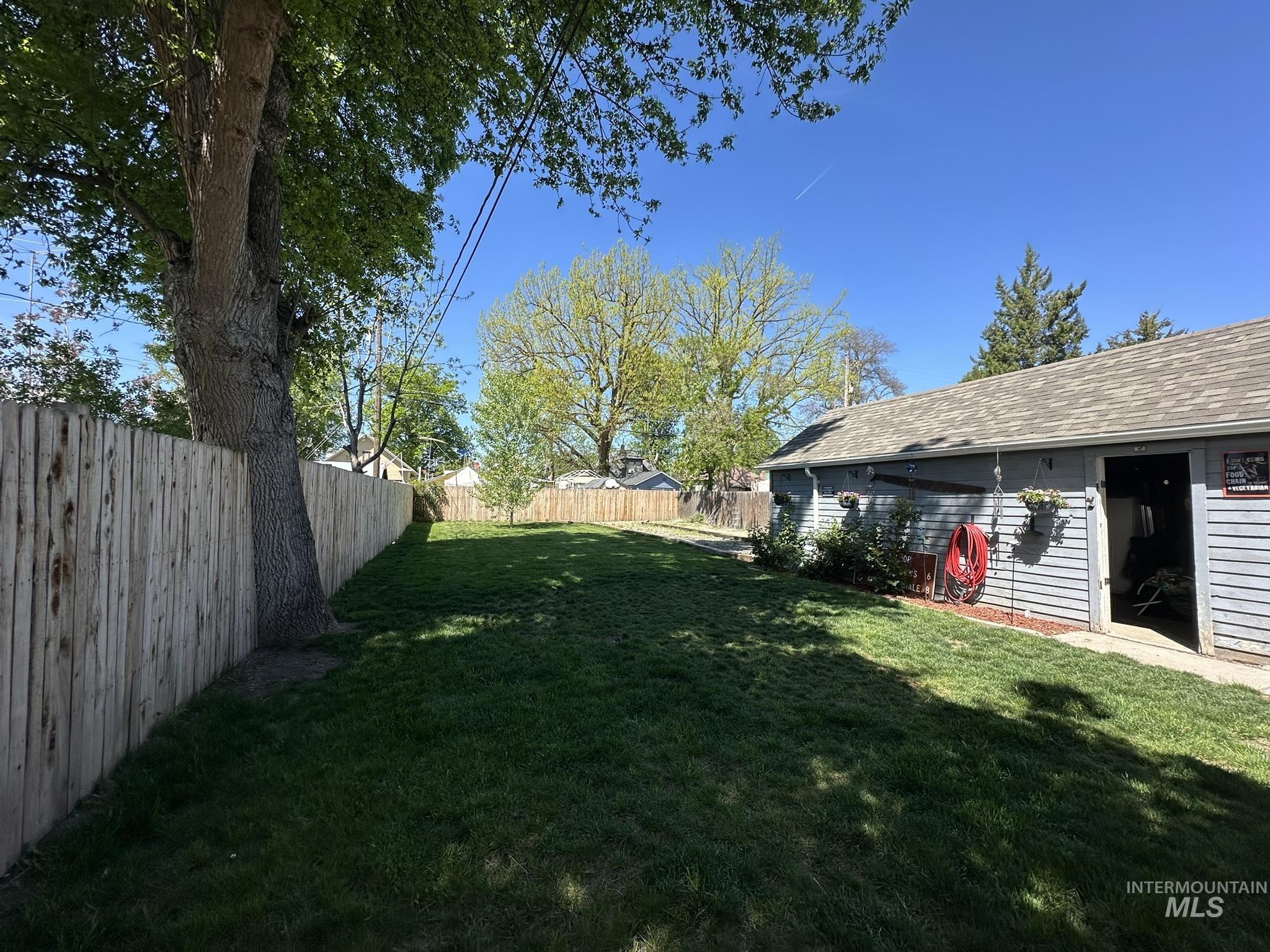 409 North 7th Street Payette, ID 83661 - Photo 16 of 23 Expansive backyard featuring a manicured lawn, established mature trees, a full privacy fence, and a detached garage with an asphalt shingle roof and horizontal siding