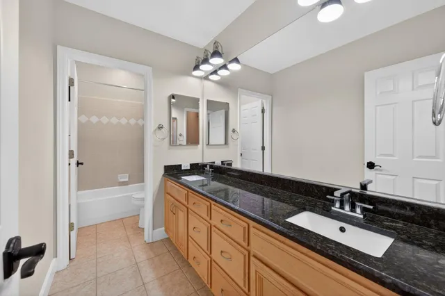 a spacious bathroom with a granite countertop double vanity sink a mirror and a bathtub
