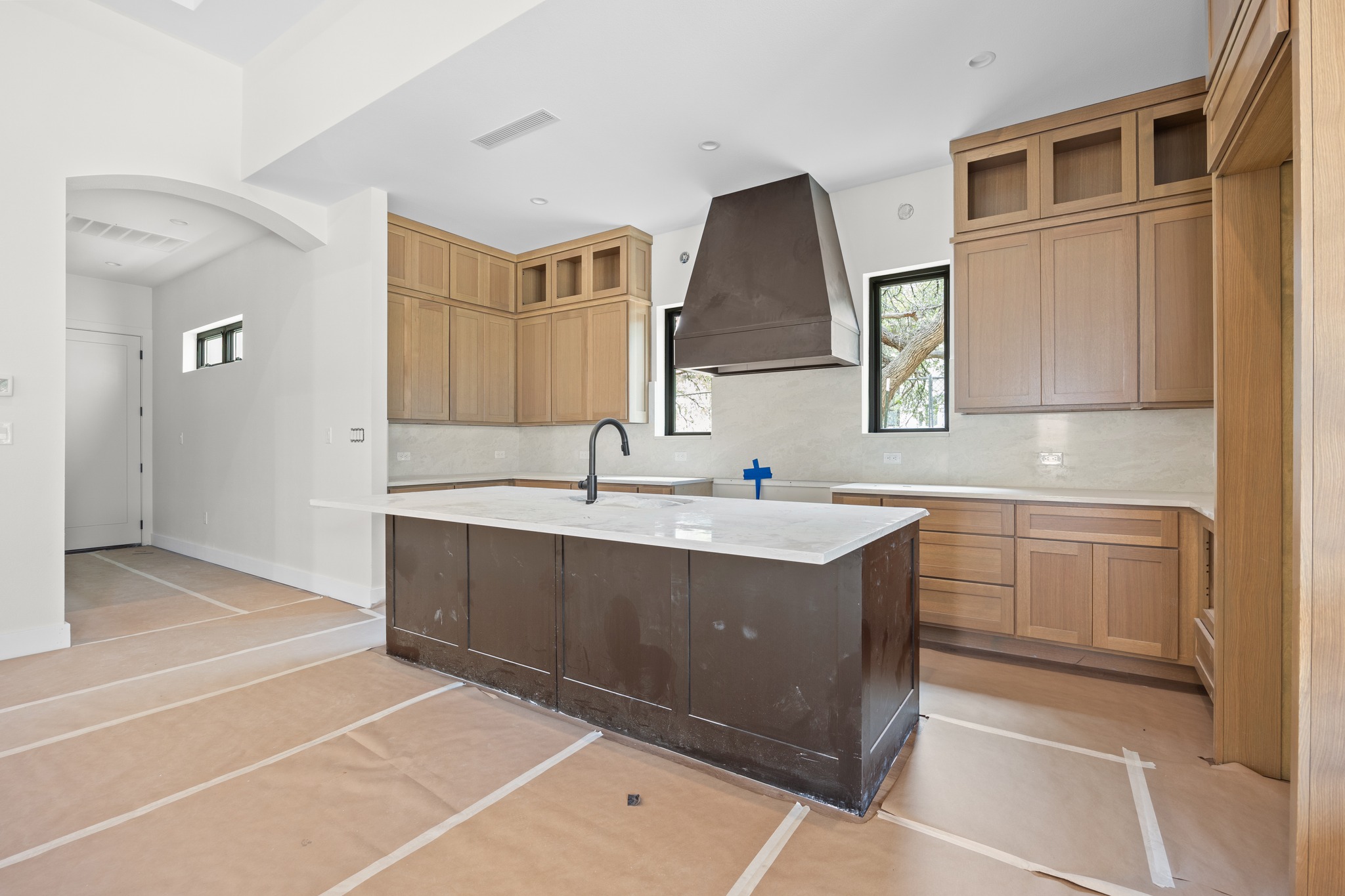 903 Flint Ridge Trail Georgetown, TX 78628 - Photo 11 of 39 Kitchen featuring a large central island with a light-toned countertop, a custom range hood, shaker-style cabinetry with upper glass-front cabinets, and a contemporary sink faucet