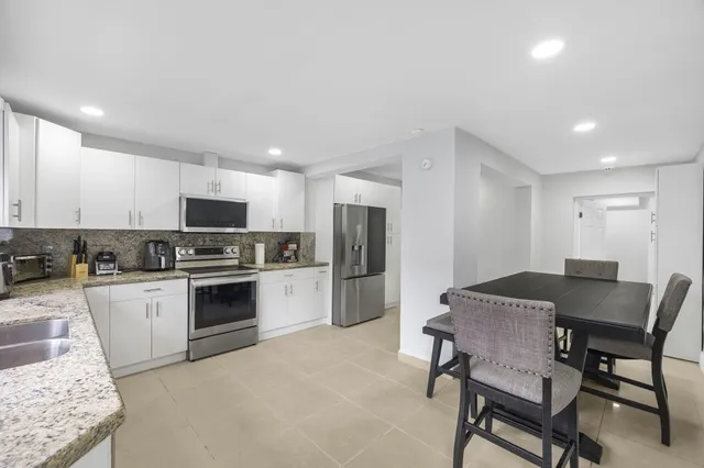 a kitchen with stainless steel appliances kitchen island granite countertop a table chairs microwave and refrigerator