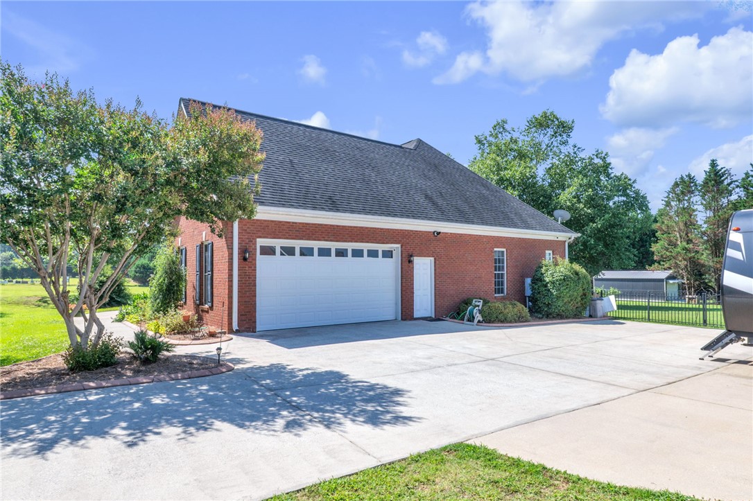 648 Mountain View Road Williamston, SC 29697 - Photo 33 of 42 A spacious driveway leads to a brick garage with a large white door, surrounded by verdant landscaping.