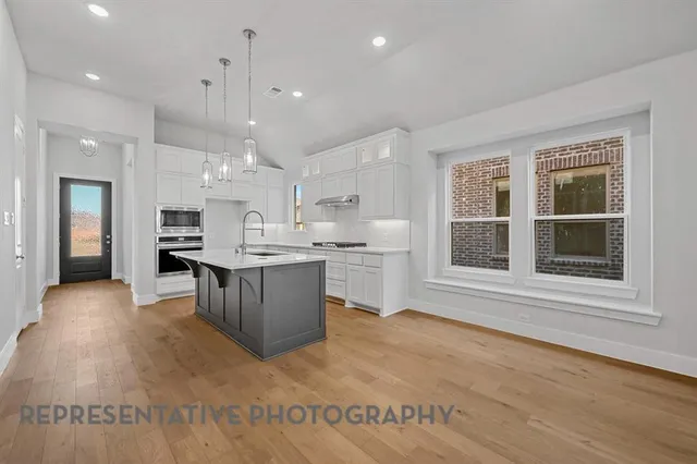 a large white kitchen with kitchen island a stove a sink a refrigerator and white cabinets with wooden floor