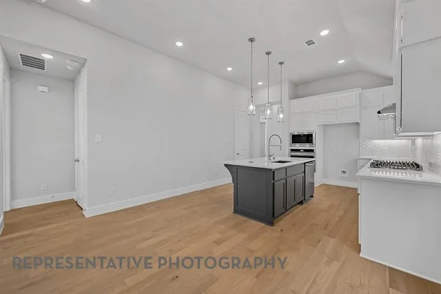 a large kitchen with kitchen island a stove a sink a refrigerator and white cabinets with wooden floor